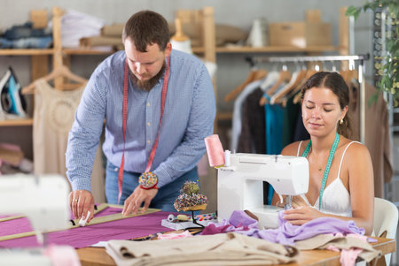Young seamstress sewing while colleague marking fabricの写真素材