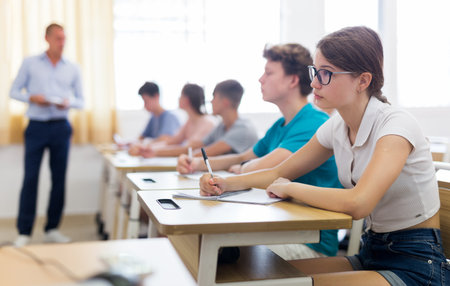 Teenagers listening to lecturer and writing in notebooksの写真素材
