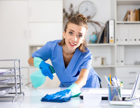 Female cleaning service worker wiping working table in officeの写真素材