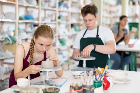 Pottery lesson - teenagers girl and guy intently create dishes from clayの写真素材