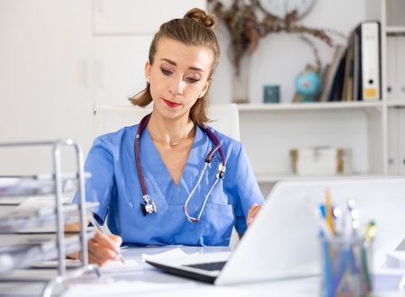 Woman doctor sitting at workplace with computer in her officeの写真素材