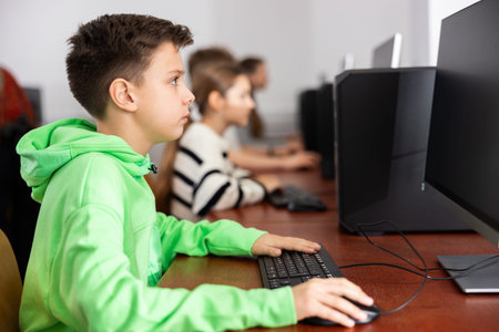 Focused tween boy studying with classmates in computer lab