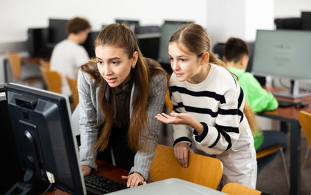 Female teacher talking to focused teen girl student in computer classの写真素材