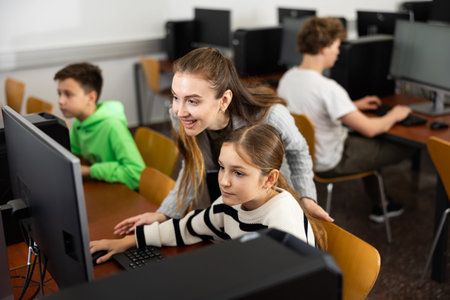 Positive woman teacher together with the girl teaches how to work on computer