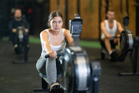Determined young girl training with rowing machine in sports hallの写真素材