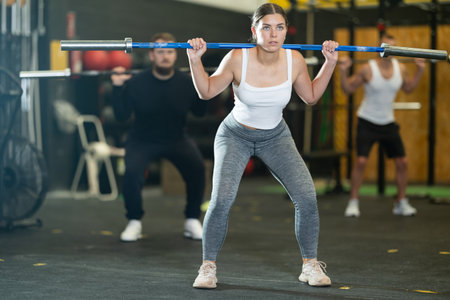 Young woman performing exercises with barbell during intense trainingの写真素材