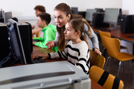 Positive woman teacher together with the girl teaches how to work on computerの写真素材