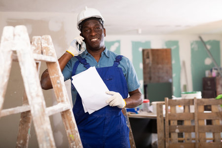 African american foreman with documents in his hands is talking on a mobile phone