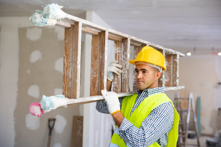 Construction worker carrying stepladder in apartment