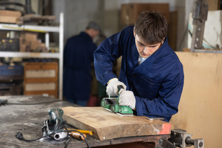 Young guy polishing wooden board in workshop