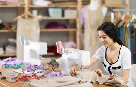 Female clothing designer stitching fabric on sewing machine in studio