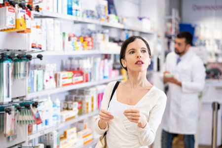 Woman chooses medical products in pharmacy, checking the list on piece of paperの写真素材