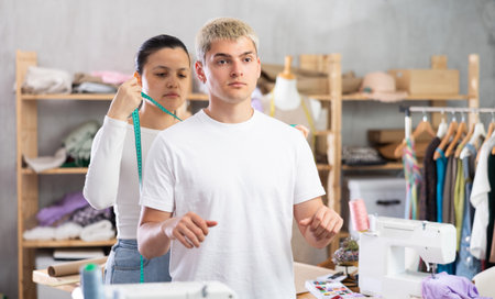 Young Asian tailoress measuring male client in sewing workshopの写真素材