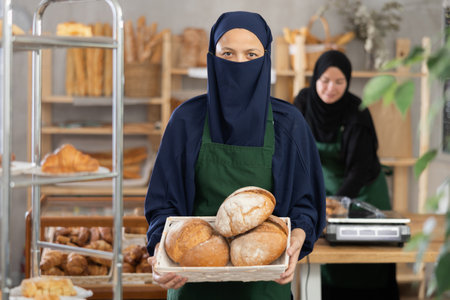 Positive woman seller of oriental bakery in niqab with fresh hot pastries in handsの写真素材