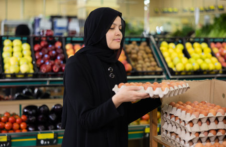 Young Asian lady in hijab in supermarket buys chicken eggs.