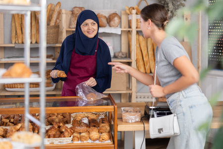 Smiling Muslim bakery worker bagging croissants for customerの写真素材