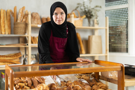 Muslim girl seller employee puts croissants in window, arranges display of goods at bakery.の写真素材
