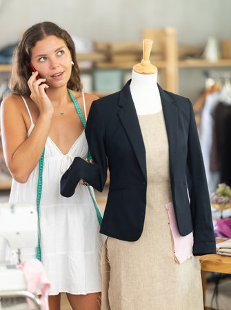 dressmaker stands near the mannequin and talks on her mobile phoneの写真素材