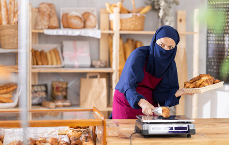 Asian Muslim woman seller in hijab weighs croissants on scale,の写真素材