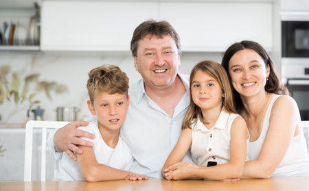 Parents posing with their two little children by the table in the kitchen