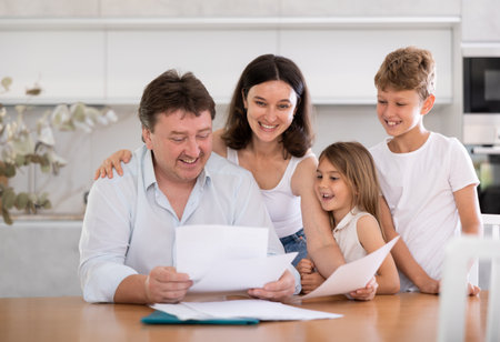 Positive husband is sitting at kitchen and reading document about career advancement at workの写真素材