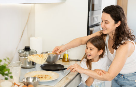 Happy mother and daughter frying pancakes in the kitchenの写真素材