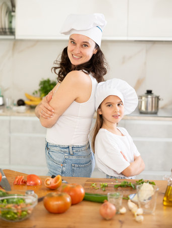 Mother and preteen daughter wearing chef hats standing at tableの写真素材