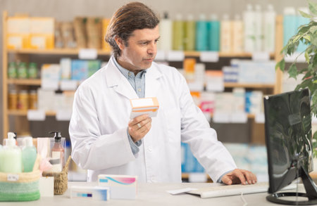 Male pharmacist looking for pills on computerの写真素材