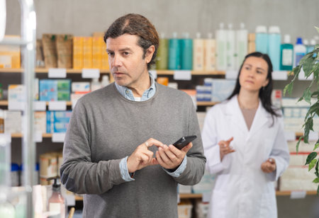Male customer looking for something in drugstore. Female pharmacist offers him medicinesの写真素材