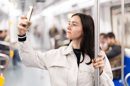 In the subway car, woman with mobile phone makes a selfie or scans QR codeの写真素材