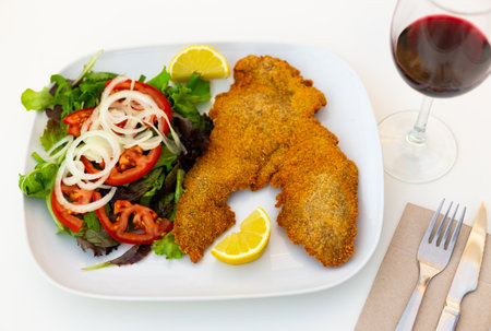 Portion of breaded cutlet, milanesa, with salad served on tableの写真素材