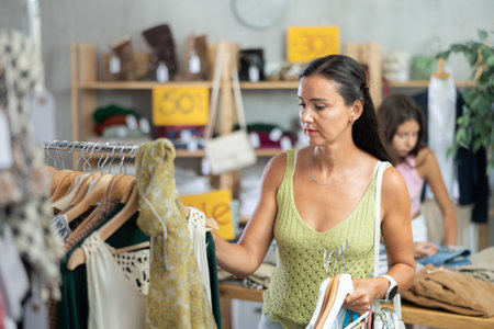 Near rack, woman buys something summer cloth, chooses items.