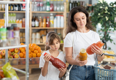 Mother and daughter choose tasty juice together in grocery section of supermarketの写真素材