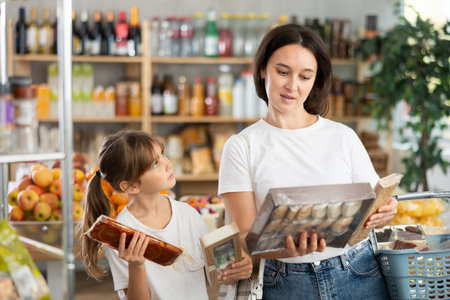 Mother consults with her daughter about which sweets to buy in the grocery section of supermarket - nougat or cookiesの写真素材