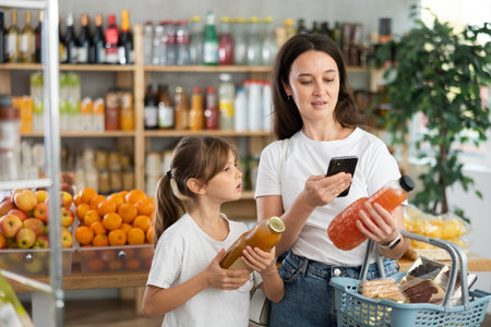 Mother and daughter choose bottles of juice and scan QR code with smartphone in supermarketの写真素材