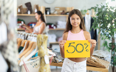 Teen girl with poster in hands announce mega 50percent discounts in womens clothing storeの写真素材