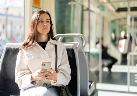 Woman is sitting in tram wagon with phone, getting to work. Woman on trip communicating on social...