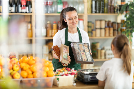 Female seller offers to buy cookies to teenage girl in interior of grocery supermarketの写真素材