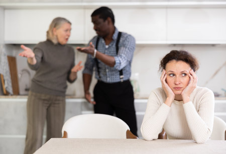 Upset woman tired of domestic quarrel. Husband and mother in law quarreling in backgroundの写真素材