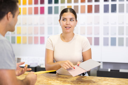 Female saleswoman of paintwork material shop advises man buyer with samples and product catalogの写真素材
