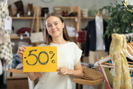 Teenage girl holding discount sign in clothing storeの写真素材