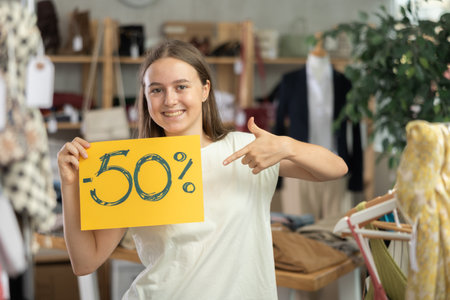 Teen girl holding sign saying 50 percent discount in clothing storeの写真素材