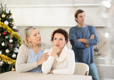 Senior woman sits near daughter and comforts during quarrel with husband on Christmas Eveの写真素材