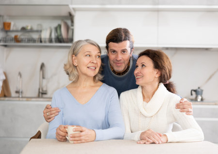 Elderly smiling woman is sitting at table with man and woman