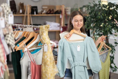 Girl chooses a set of clothes for summer. Visitor to the boutique examines the new summer collection of clothesの写真素材
