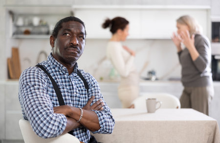 Adult sad man sitting at table during family quarrelの写真素材