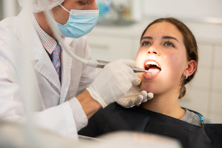 Adult male dentist cleaning teeth of female patientの写真素材