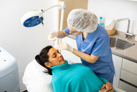 Woman cosmetician giving face injections of botulinum toxin for young womanの写真素材