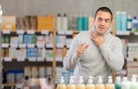 Young man with sore throat and cough at pharmacyの写真素材
