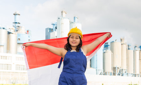 National flag of Indonesia in the hands of girl in overalls against background of modern metallurgical plantの写真素材